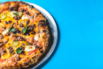 Whole cheese and meat pizza over blue background. Pizza with onions and pickles served on a metal tray.