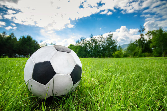 Football soccer ball on green grass field on summer sky background with copy space