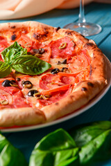 Fresh italian pizza with salami and black olives and other food on the background. Blue colored wooden table.