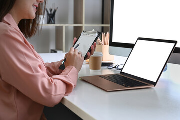 Cropped shot businesswoman holding clipboard and working with laptop at office.
