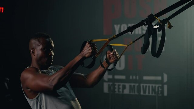 Black muscular man during exercise training workout bodyweight with suspension straps TRX pull ups training arms at stylish empty gym center fitness GYM, workout healthy lifestyle sport concept