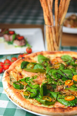 Delicious pizza with spinach and tuna shavings served on wooden table with green plaid tablecloth.