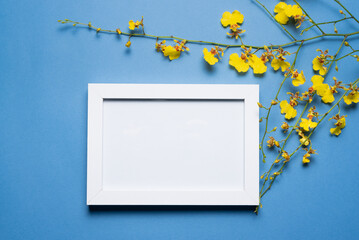Blank empty picture frame with copy space and oncidium orchid flowers branch on the blue flat lay background.