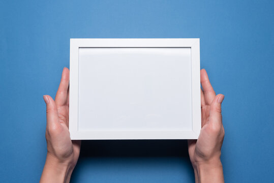 Blank empty picture frame with copy space in the female hands flat lay background.