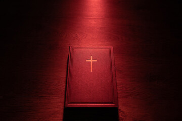 Closed bible on a wooden table with light coming from above. Catholic cross on cover of bible....