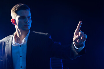 Business man pushing imaginary button. Young business man in classic suit. Human on a dark background. He reaches out to screen. Guy clicks on virtual screen. Man stretches his finger to monitor