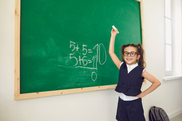 Back to school. A schoolgirl with glasses writes on a school board in a classroom at a lecture....