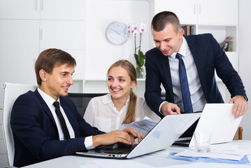 Fototapeta premium Three smiling business male and female assistants in formalwear holding paper documents and chatting in company office