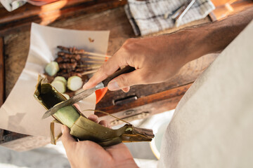 close up of sate ayam preparation served with rice cake or lontong with peanut sauce on food paper