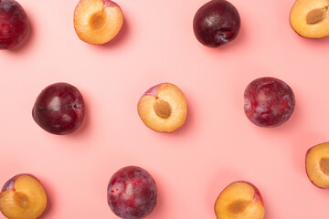 Top view photo of halves and whole plums on isolated pastel pink background