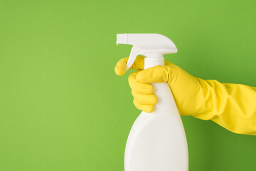 Above photo of cleaning spray and hands in yellow gloves isolated on the green background