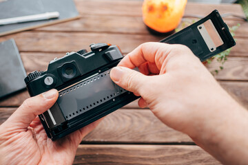 Photographer inserts analog film into camera on wooden table.