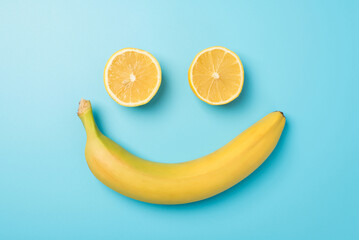 Top view photo of smiling face made from two lemon halves and yellow banana on isolated light blue...