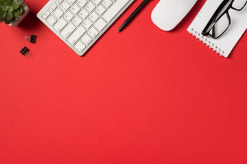 Top view photo of white keyboard mouse plant black pen binder clips and glasses on spiral copybook...