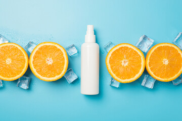 Top view photo of white spray bottle without label sliced oranges and ice cubes in raw on isolated pastel blue background with blank space