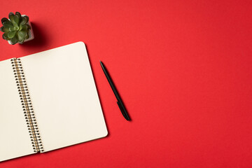 Top view photo of flowerpot pen and open spiral notebook on isolated vivid red background with blank space