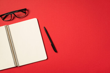 Top view photo of black glasses pen and open spiral notebook on isolated vivid red background with...