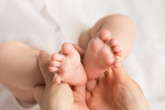 Closeup photo of mother's hands holding baby's small feet on isolated white cloth background