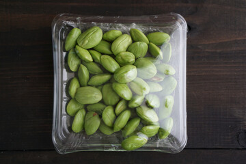 Bitter bean, twisted cluster bean, or stink bean wrapped in plastic on a black wooden table. In...