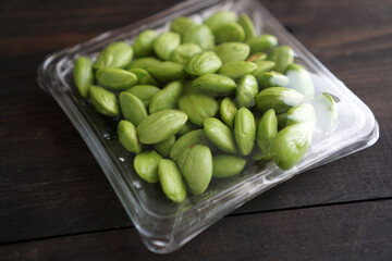 Bitter bean, twisted cluster bean, or stink bean wrapped in plastic on a black wooden table. In Indonesia its called 