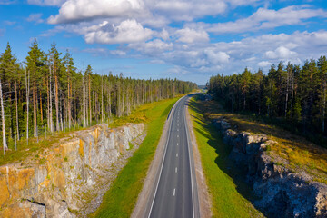 Road in Karelia. Russia. An empty highway from a drone. Travel, voyage, vacation. The road goes over the horizon. Summer travel. A country road with rocky verges. Highway among the pines.