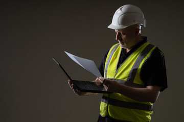 Fototapeta premium An architect or engineer with a laptop and drawings. The construction engineer clarifies the details of the project. Technical specialist with a laptop. An engineer in a white helmet.