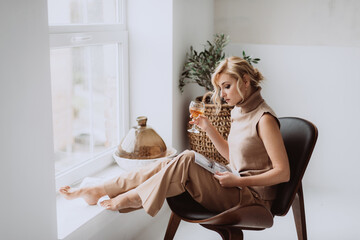 Young businesswoman works at home. Pensive calm model holds a glass of white wine and reads a magazine. Beautiful woman in a modern interior. Soft selective focus.