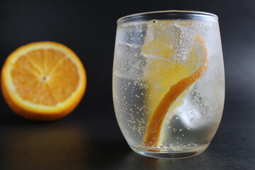 lemonade with orange and ice in a glass on a black background next to lies ice and orange. Summer drink on a black background