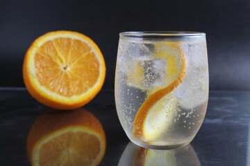 lemonade with orange and ice in a glass on a black background next to lies ice and orange. Summer drink on a black background