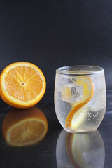 lemonade with orange and ice in a glass on a black background next to lies ice and orange. Summer drink on a black background