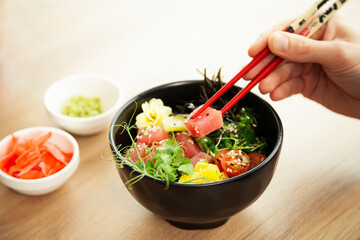 A man eats a Poke salad with tuna in a bowl with chopsticks. Place the tuna salad in a bowl. Young man guy in a restaurant eating poke salad. Asian seafood salad concept.