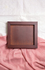The wooden empty frame lies on the pink fabric with folds, the view from above. Vertical.