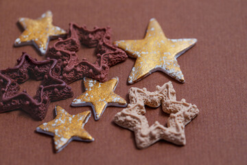 Fototapeta na wymiar Gold and chocolate stars on a brown craft background. Handmade polymer clay miniatures. 