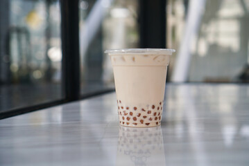 Iced Milk Tea with golden bubble. A plastic cup of milk tea with bubble/boba (golden pearl) on table.