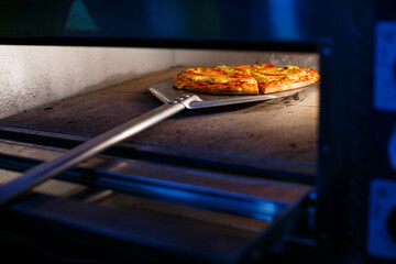 Hot tasty American pizza with tomato cheese and meat with a thick crust on a metal shovel, the baker takes out the pizza from the oven