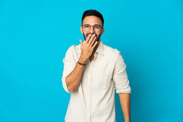 Young caucasian man isolated on blue background happy and smiling covering mouth with hand