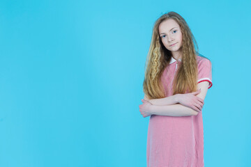 Still Teenager Blond Girl in Long Red Checked Dress With Folded Hands Against Blue Background.