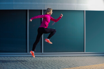 Mature Woman Running in High Jump Outdoors Against Glass Reflective Background.