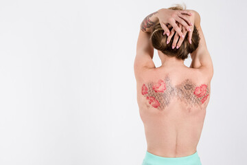 Back of Young Caucasian Brunette Woman With Flowery Tattoes on Her Back Posing With Lifted Hands On White.
