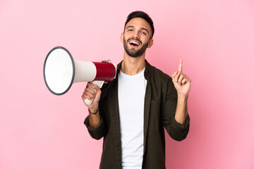 Young caucasian man isolated on pink background holding a megaphone and pointing up a great idea