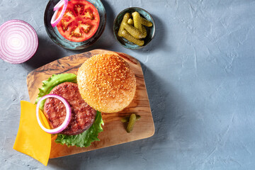 Burger ingredients with copy space, shot from above. Hamburger beef patty, Cheddar cheese, red onion, tomato slice, sesame bread buns and pickles