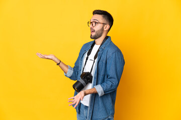 Young photographer girl isolated on yellow background with surprise expression while looking side