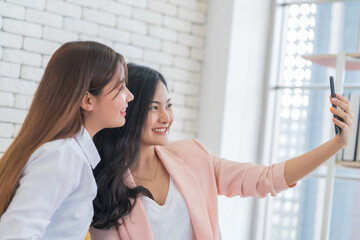 Beautiful young business women are selfie with her friend by cellphone or smartphone at living room. Happy friendship relationship concept