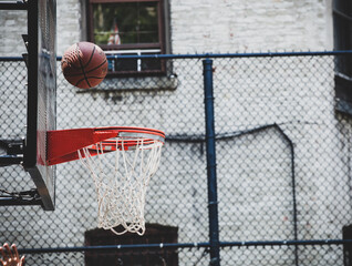 Basketball hoop in a neighborhood playing field in New Yor. The ball bounces off the board ready to...