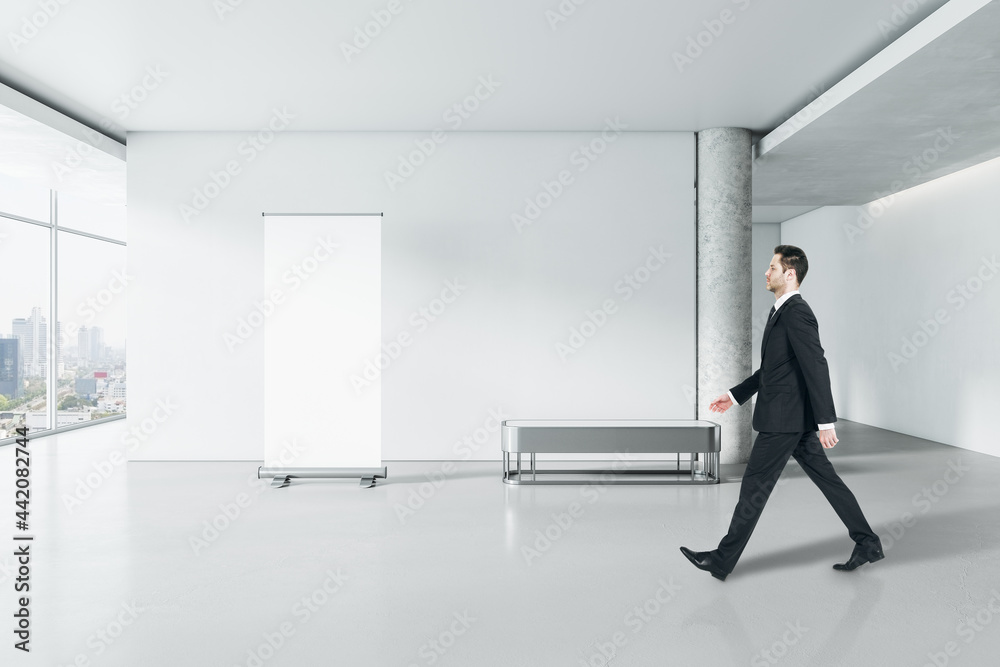 Poster businessman walking in modern gallery interior with empty poster on concrete wall and window with ci