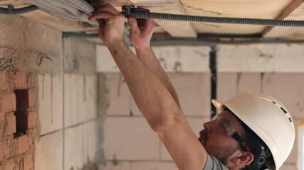 Fixing plastic tubes for electrical wires in the ceiling in wiring system on unfinished construction site. - Powered by Adobe