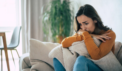 Sad woman in deep depression is sitting on the couch and crying and thinking about the bad thing - obrazy, fototapety, plakaty