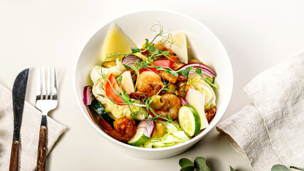 Food banner summer salad with fresh vegetables, fried shrimps, cheese and herbs. Seasonal vegetables, seafood and goat cheese. Appetizing healthy Mediterranean food and diet. Cutlery. Top view