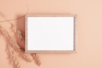 Photo frame, dried grass decoration on beige background. Invitation card mockup on beige table. Flat lay, top view, copy space, mockup