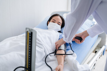 Obraz premium Young woman lying on the hospital bed wearing a mask for checking blood pressure during the outbreak of the coronavirus 19. Concepts to prevent the spread of COVID-19.